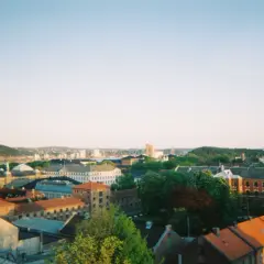 Widok na centrum Oslo z dachu kamienicy. Słońce zachodzi nad miastem, rzucając ciepłe światło na dachy i fasady budynków.