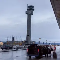 Wieża kontrolna na lotnisku w Norwegii. Samochody i ludzie przy terminalu, deszczowa pogoda.