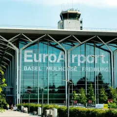 Nowoczesny budynek EuroAirport Basel Mulhouse Freiburg. Szklana fasada z napisem lotniska i wieża kontroli lotów.