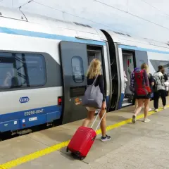 Dziewczyny z plecakami i walizką wsiadają do pociągu PKP. Warto wiedzieć, jak kupić bilet na pociąg, by podróżować bez stresu.