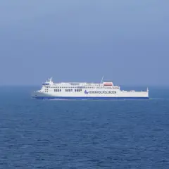 Prom, który ułatwia dojazd z Polski, płynie po spokojnym morzu. Obok żaglówka.