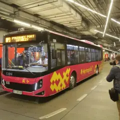 Różowy autobus linii AP3 z napisem "Pyrzowice Port Lotniczy" wjeżdża na pętlę. Obok stoi fotograf z aparatem. Bilety Katowice można kupić na pokładzie.