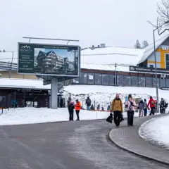 Zimowy dzień w Karpaczu, Świeradowie-Zdroju. Ludzie spacerują przy stoku narciarskim, obok billboardu reklamującego apartamenty.
