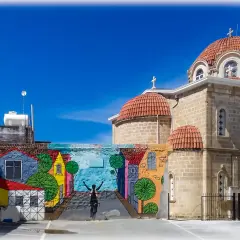 Kolorowy mural z rowerzystą i domkami na tle kościoła z kopułami. Pafos stare miasto.