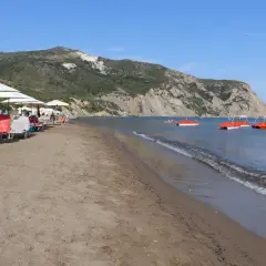 Słoneczny dzień na plaży Kalamaki. Leżaki pod parasolami, spokojne morze i czerwone rowery wodne.