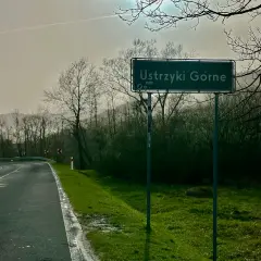 Znak drogowy "Ustrzyki Górne" na tle mglistego krajobrazu z krętą drogą i drzewami.