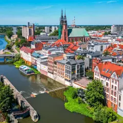 Widok na Opole z rzeką i grodem. Słoneczny dzień nad Odrą, widać kościół i kamienice.