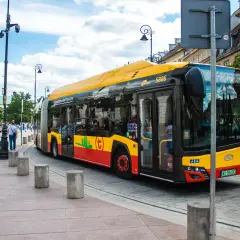 Żółto-czerwony autobus miejski, symbol darmowej komunikacji miejskiej, jedzie ulicą.