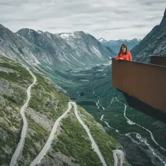 Kobieta na platformie widokowej podziwia serpentyny drogi Trollstigen w otoczeniu gór.