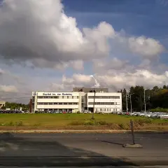 Szpital im. Św. Rodziny, dojazd autobusem. Budynek szpitala z parkingiem i zielenią.