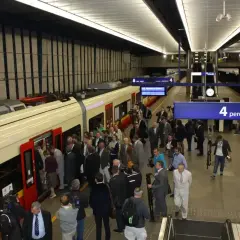 Ludzie wsiadają do pociągu na stacji Warszawa Centralna. Tablica informuje o peronie 4, który obsługuje połączenie do Lotniska Chopina.