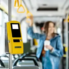 Żółty biletomat MPK Kraków w pojeździe komunikacji miejskiej. W tle rozmyta pasażerka z kubkiem kawy.