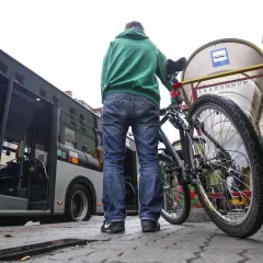 Mężczyzna z rowerem czeka na autobus. Rower stoi obok niego przy przystanku.