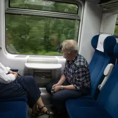 Starsza para podróżuje pociągiem, ciesząc się widokami za oknem. Korzystają ze zniżek na pociąg dla emerytów.