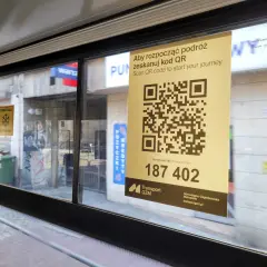 W autobusie widoczny jest żółty plakat z kodem QR i napisem "Aby rozpocząć podróż zeskanuj kod QR". Pod kodem znajduje się numer 187 402.