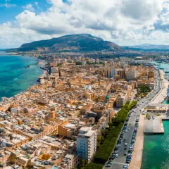 Widok na Trapani z lotniska: miasto, port z wycieczkowcem i żaglowcem, góry w tle.