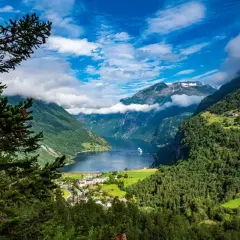 Majestatyczne fiordy Norwegii, zielone zbocza gór, błękitne niebo z chmurami i biały statek na wodzie.