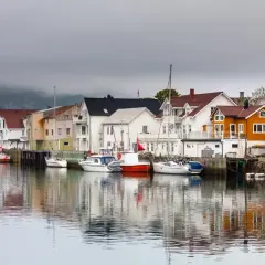 Kolorowy port w Norwegii z domkami i łodziami odbijającymi się w spokojnej wodzie.