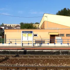 Peron kolejowy w Starachowicach z tablicą informacyjną i budynkiem dworca w tle.