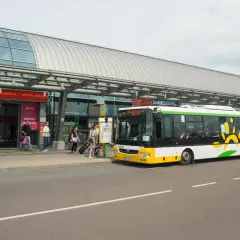Autobus z logo Modlin Airport czeka na pasażerów przy terminalu.