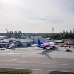 Samolot Wizz Air na płycie lotniska Sztokholm Skavsta. W tle budynki terminali i wieża kontroli lotów.