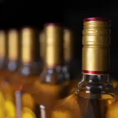 Rząd butelek z bursztynowym płynem, każda z złotą zakrętką i czerwoną obrączką. Zastanawiasz się, ile alkoholu do uk?