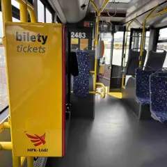 Wnętrze autobusu MPK-Łódź. Żółta skrzynka z napisem "bilety tickets" i logo MPK-Łódź. Widoczne siedzenia i poręcze.