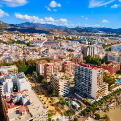 Widok z lotu ptaka na słoneczne miasto Malaga Marbella, z górami w tle i plażą pełną leżaków.