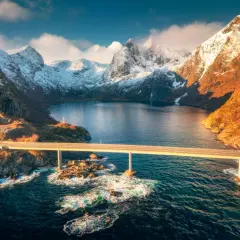 Most majestatyczny fiord w Norwegii, z mostem przecinającym turkusową wodę i ośnieżonymi górami w tle.