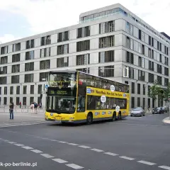 Żółte piętrowe autobusy kursują po Berlinie, mijając nowoczesne budynki.
