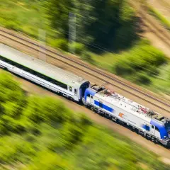 Pociąg PKP Intercity pędzi przez zielone krajobrazy. Szybko kupisz bilet na podróż przez aplikację do zakupu biletów PKP.
