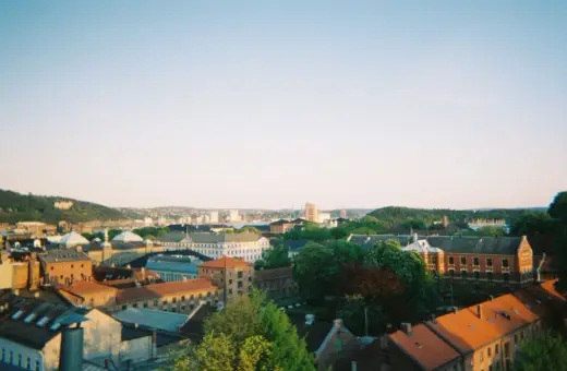 Widok na centrum Oslo z dachu kamienicy. Słońce zachodzi nad miastem, rzucając ciepłe światło na dachy i fasady budynków.