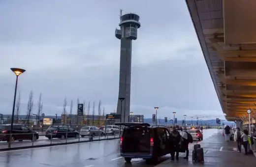 Wieża kontrolna na lotnisku w Norwegii. Samochody i ludzie przy terminalu, deszczowa pogoda.