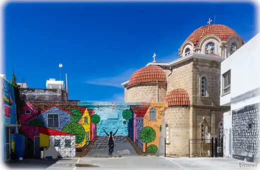 Kolorowy mural z rowerzystą i domkami na tle kościoła z kopułami. Pafos stare miasto.