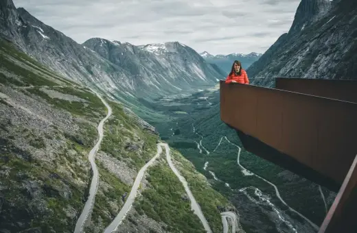 Kobieta na platformie widokowej podziwia serpentyny drogi Trollstigen w otoczeniu gór.