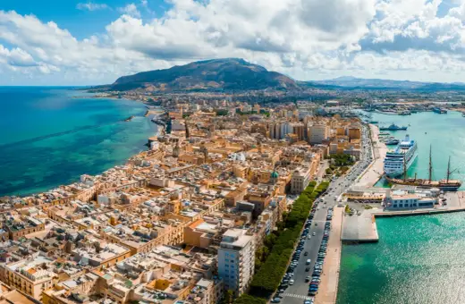 Widok na Trapani z lotniska: miasto, port z wycieczkowcem i żaglowcem, góry w tle.