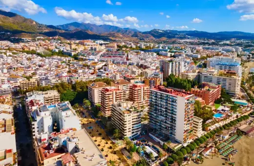 Widok z lotu ptaka na słoneczne miasto Malaga Marbella, z górami w tle i plażą pełną leżaków.