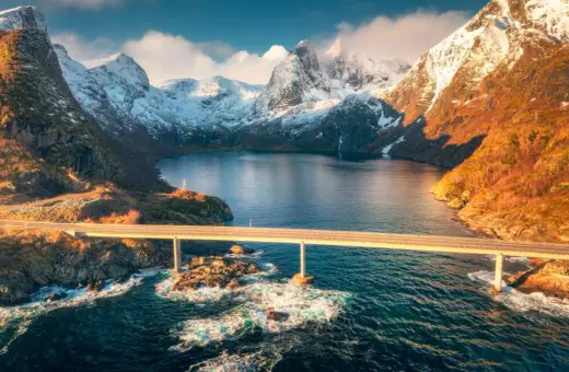 Most majestatyczny fiord w Norwegii, z mostem przecinającym turkusową wodę i ośnieżonymi górami w tle.