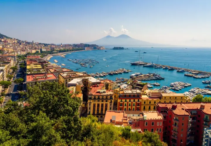 Widok na Zatokę Neapolitańską z Wezuwiuszem w tle. Miasto rozciąga się wzdłuż wybrzeża, a port pełen jest łodzi. Roma Napoli to marzenie wielu podróżników.
