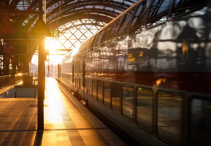 Złote światło wschodu słońca oświetla peron i pociąg PKP. Widok na dworzec kolejowy z pociągiem dwupoziomowym.