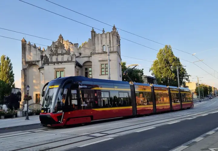 Nowoczesny tramwaj pabianice z czerwono-żółtymi pasami jedzie w stronę zabytkowego budynku.
