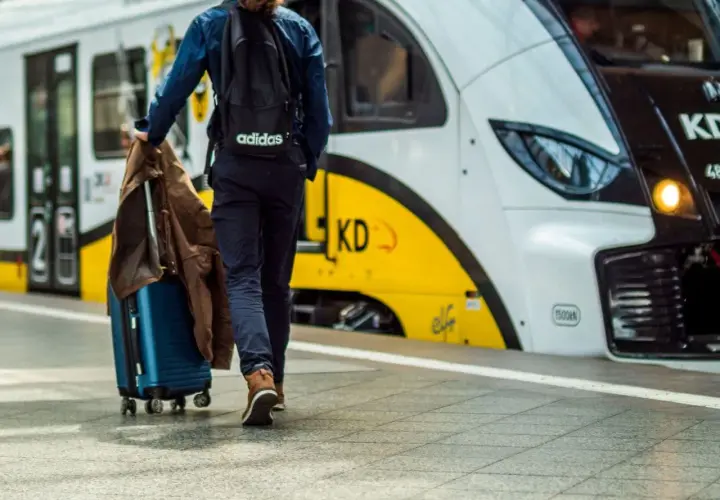 Podróżny z walizką i kurtką idzie na pociąg. Może to być podróż z Warszawy do Gdyni.