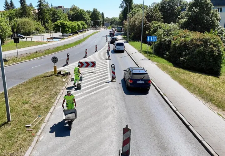 Prace drogowe na linii 101 w Szczecinie. Robotnicy w kamizelkach odblaskowych układają nawierzchnię, jeden z nich pcha taczkę z materiałem.