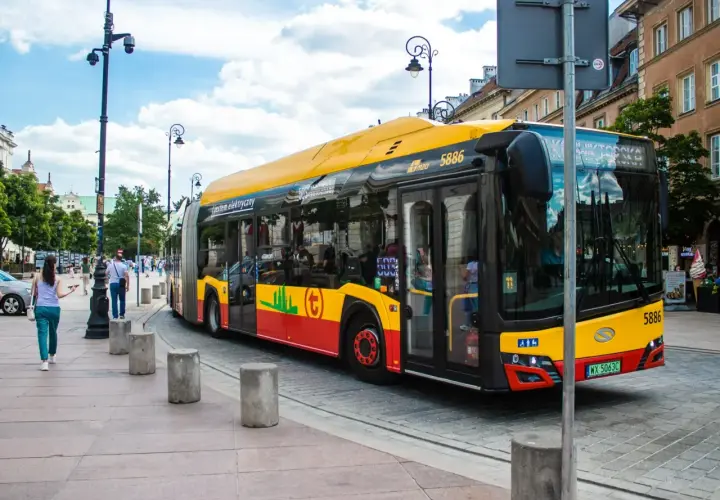 Żółto-czerwony autobus miejski, symbol darmowej komunikacji miejskiej, jedzie ulicą.