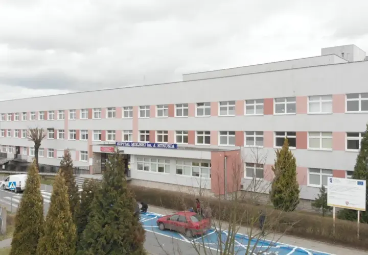 Szpital Miejski im. J. Strusia w Poznaniu. Szukasz informacji, jak dojechać do szpitala na Szwajcarskiej w Poznaniu? Budynek z wieloma oknami, przed którym rosną drzewa.