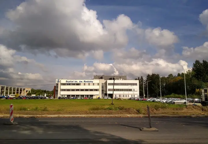 Szpital im. Św. Rodziny, dojazd autobusem. Budynek szpitala z parkingiem i zielenią.