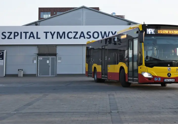 Żółto-czerwony autobus MPK z napisem "W SŁUŻBIE DLA ZDROWIA" dojeżdża do Szpitala Tymczasowego we Wrocławiu przy ul. Borowskiej.