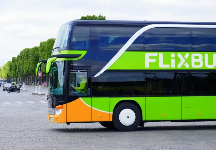 Zielony autokar FlixBus jedzie ulicą. Kierowca w żółtej kurtce prowadzi pojazd. Czy FlixBus robi postoje? Tak, ten autokar na pewno zatrzymuje się na trasie.