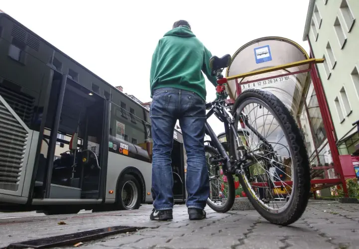 Mężczyzna z rowerem czeka na autobus. Rower stoi obok niego przy przystanku.