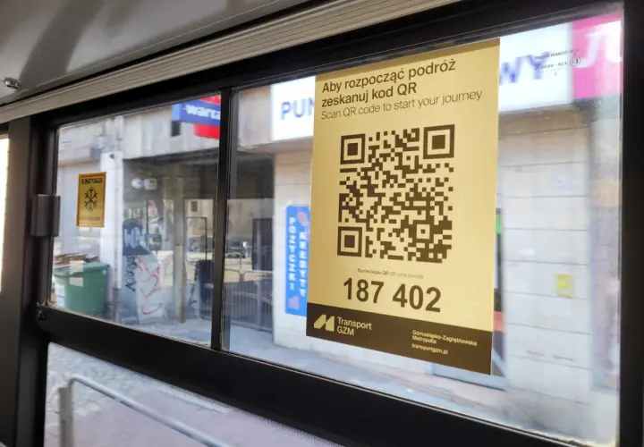 W autobusie widoczny jest żółty plakat z kodem QR i napisem "Aby rozpocząć podróż zeskanuj kod QR". Pod kodem znajduje się numer 187 402.